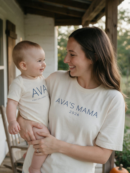 Mom holding baby on a porch, both in cream tees printed with the baby name